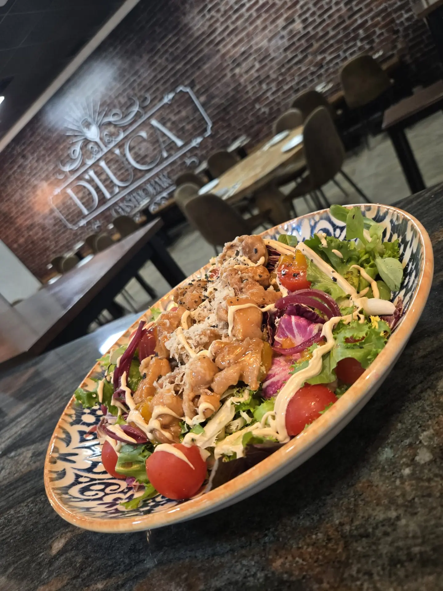 Ensalada de pollo servida en fuente de cerámica azul frente al logotipo de D'Luca