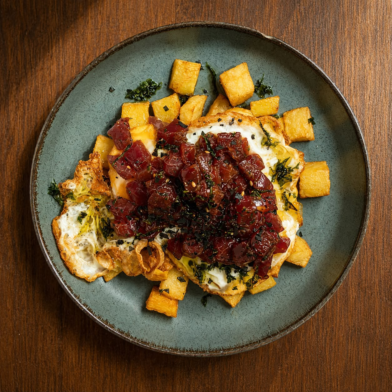 Huevos rotos con patatas y tartar de atún rojo servidos en plato de cerámica verde
