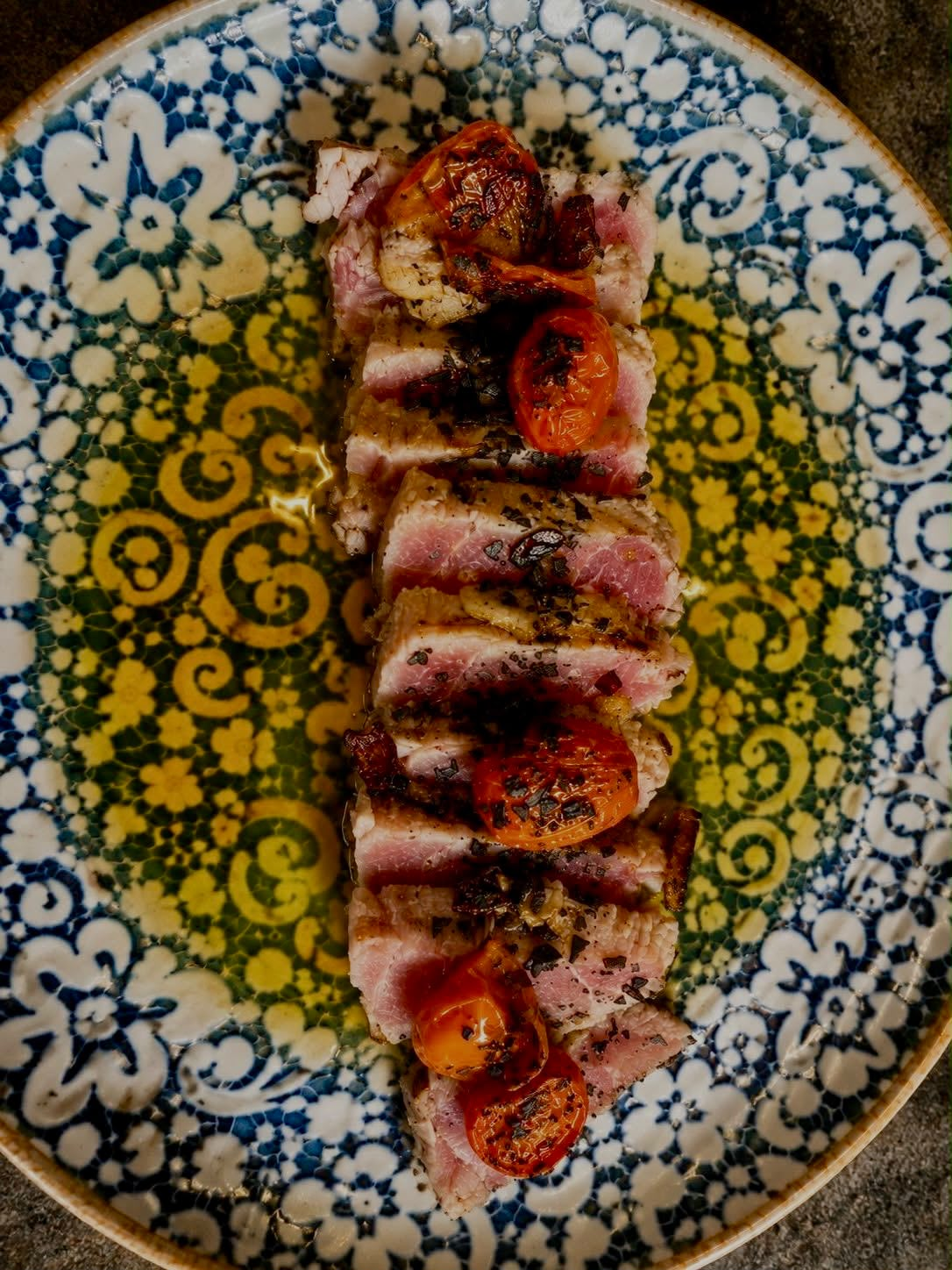 Presa ibérica a la brasa laminada con tomates cherry asados sobre plato de cerámica andaluza